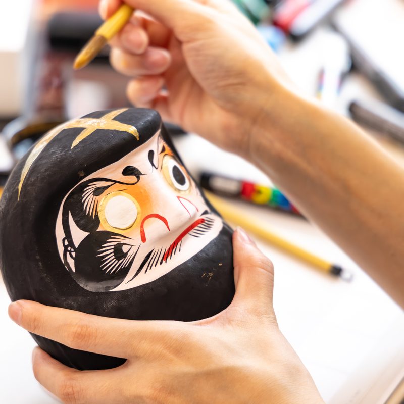 Painting gold lines on a black Daruma with a fine brush
