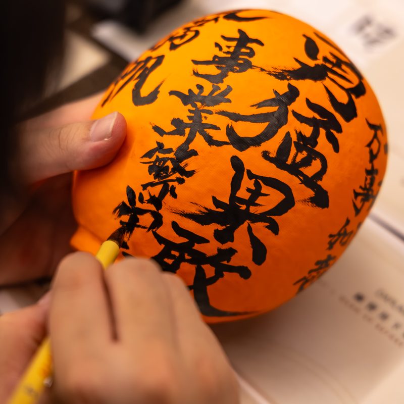 Writing kanji wishes in black ink on an orange Daruma