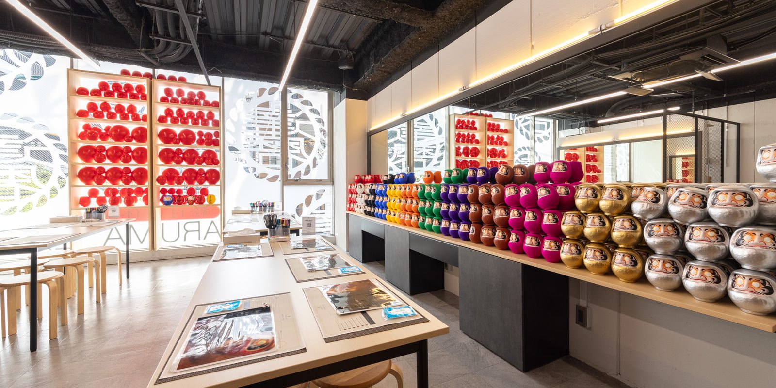 Inside DARUMA LAB. in Shinsaibashi, Osaka: painting tables in front of shelves of Daruma in twelve colours
