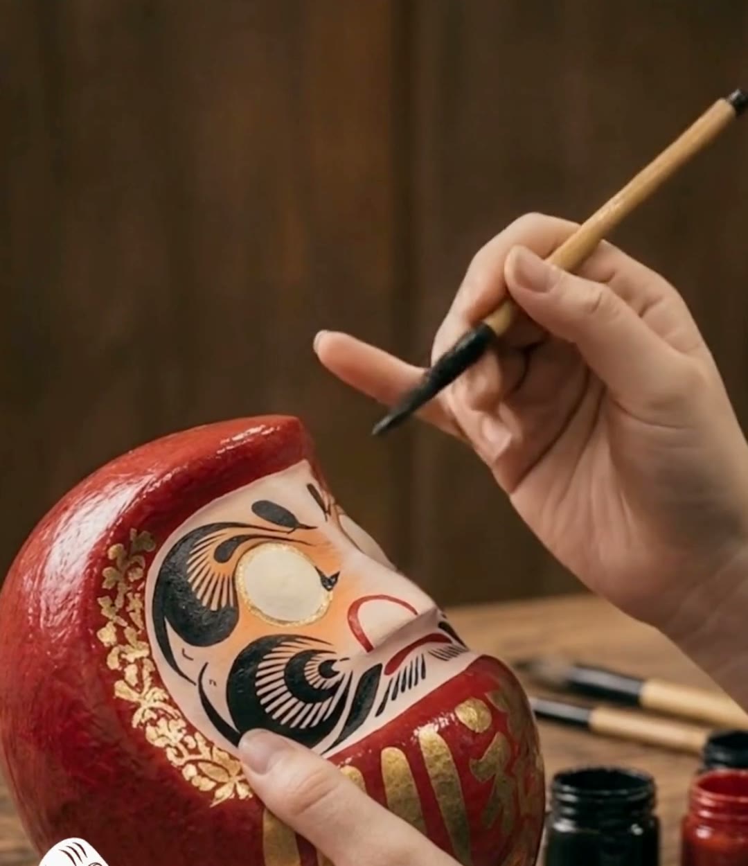 Hands painting a red Daruma with a fine brush