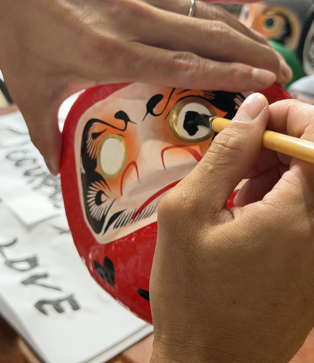 Painting in the eye of a red Daruma doll with a fine brush