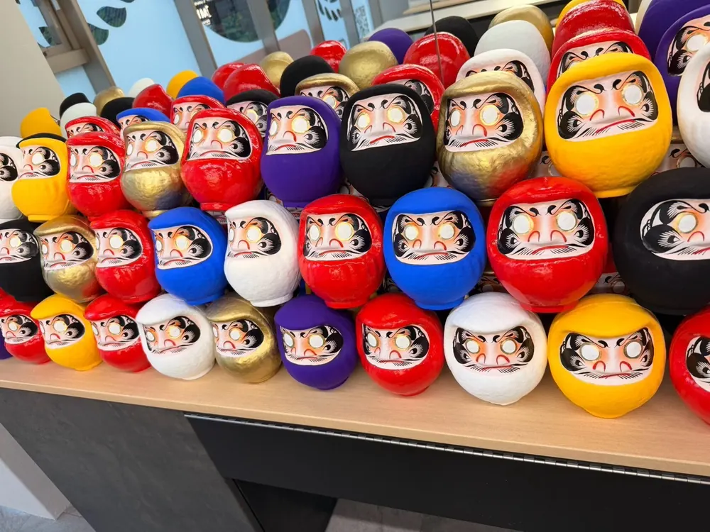 Rows of hand-painted Daruma dolls in red, blue, gold, purple and white on the shelf at DARUMA LAB. in Shinsaibashi, Osaka