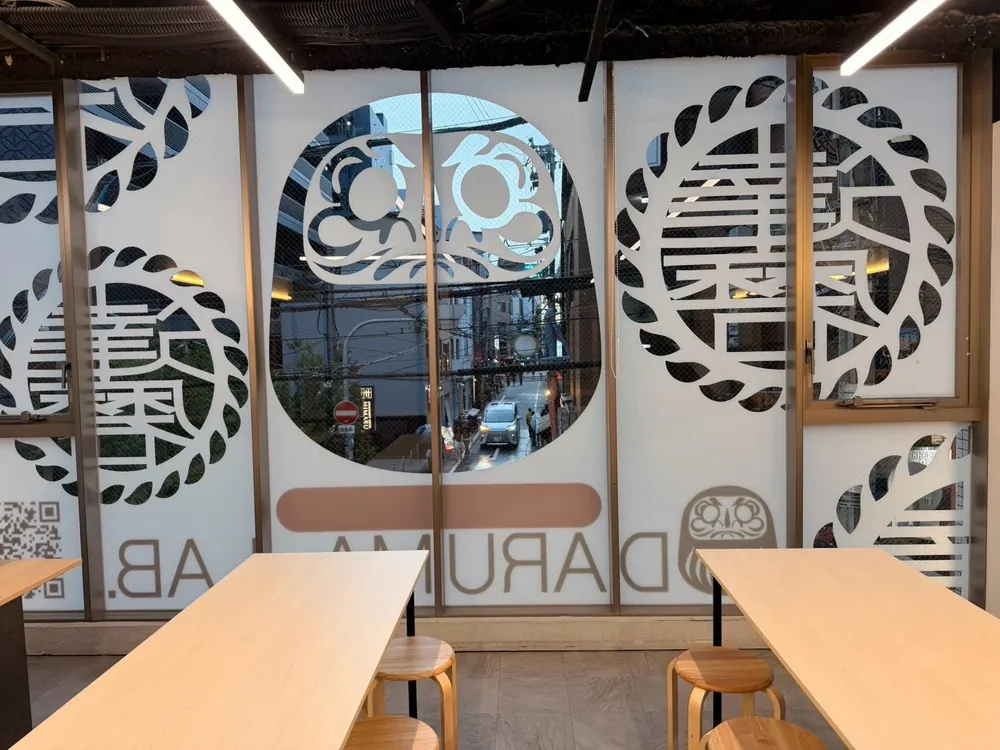 DARUMA LAB. 心斎橋店の店内。木の作業テーブルと、通りに面しただるまの窓グラフィック